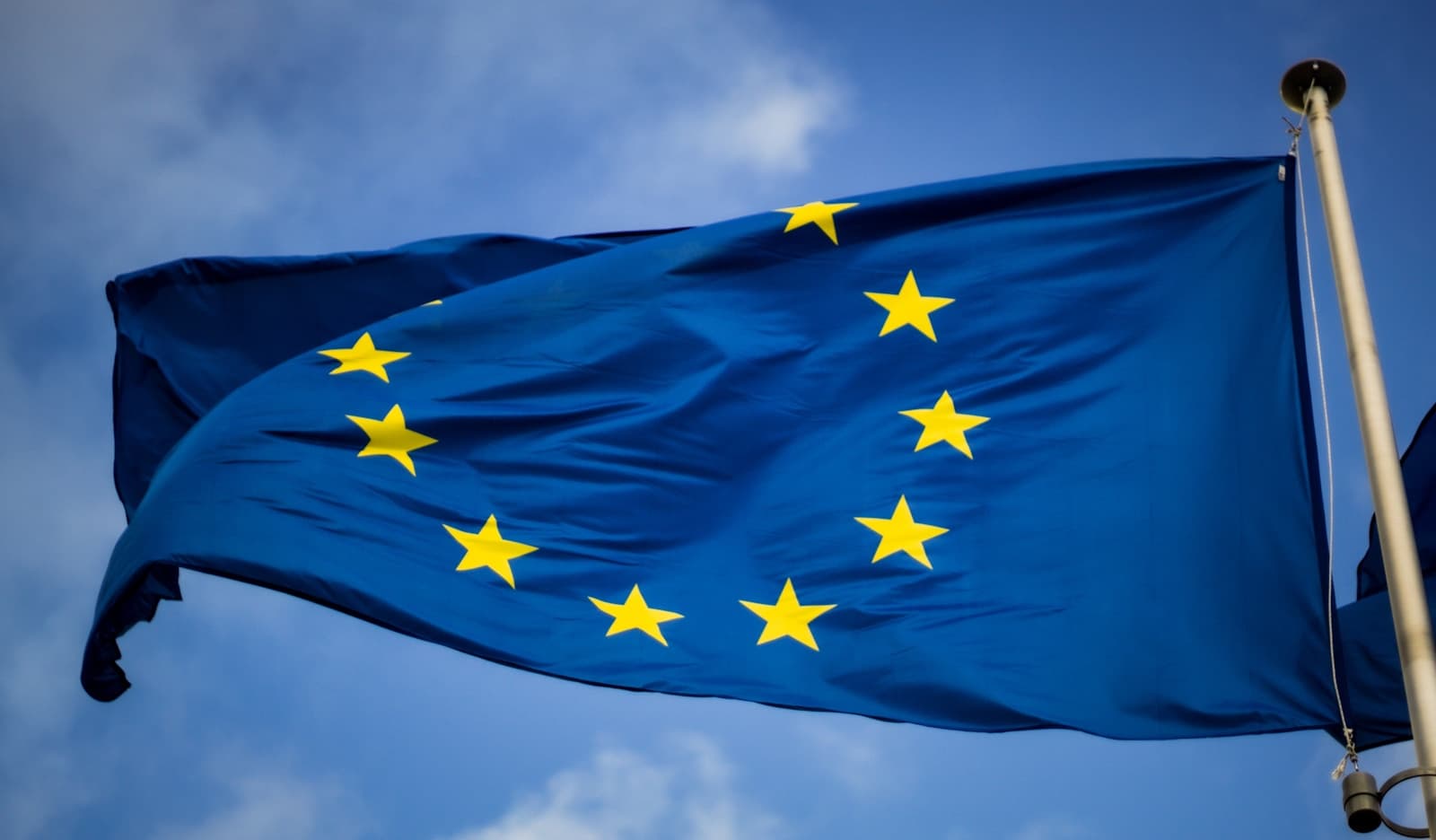 Flaga Unii Europejskiej przed budynkiem Parlamentu Europejskiego w Brukseli, fot. Christian Lue / Unsplash